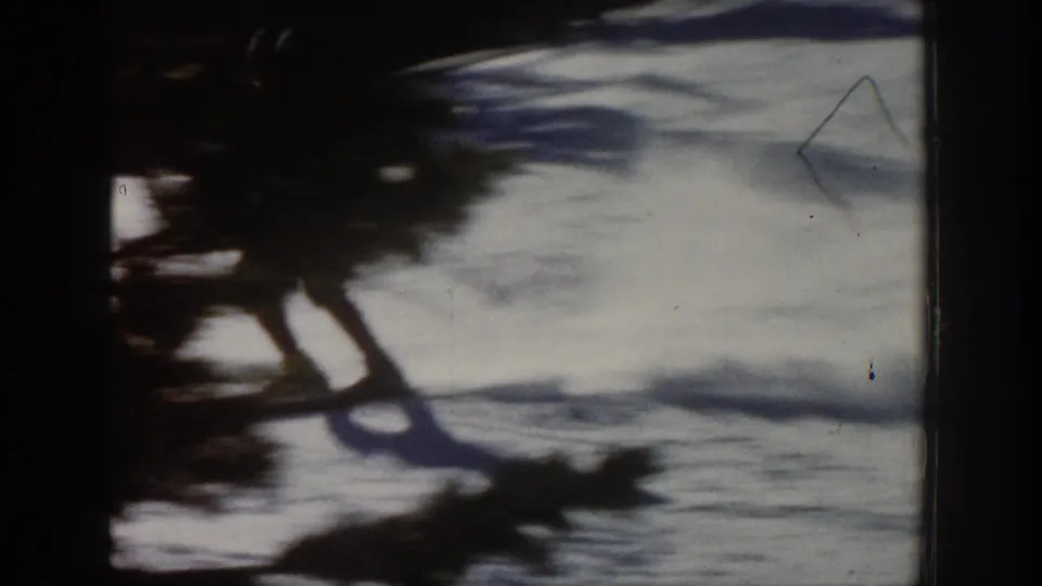 1961 Aspen 8mm frame showing a skier in dark winter clothing crossing bright snow with a long shadow nearby.