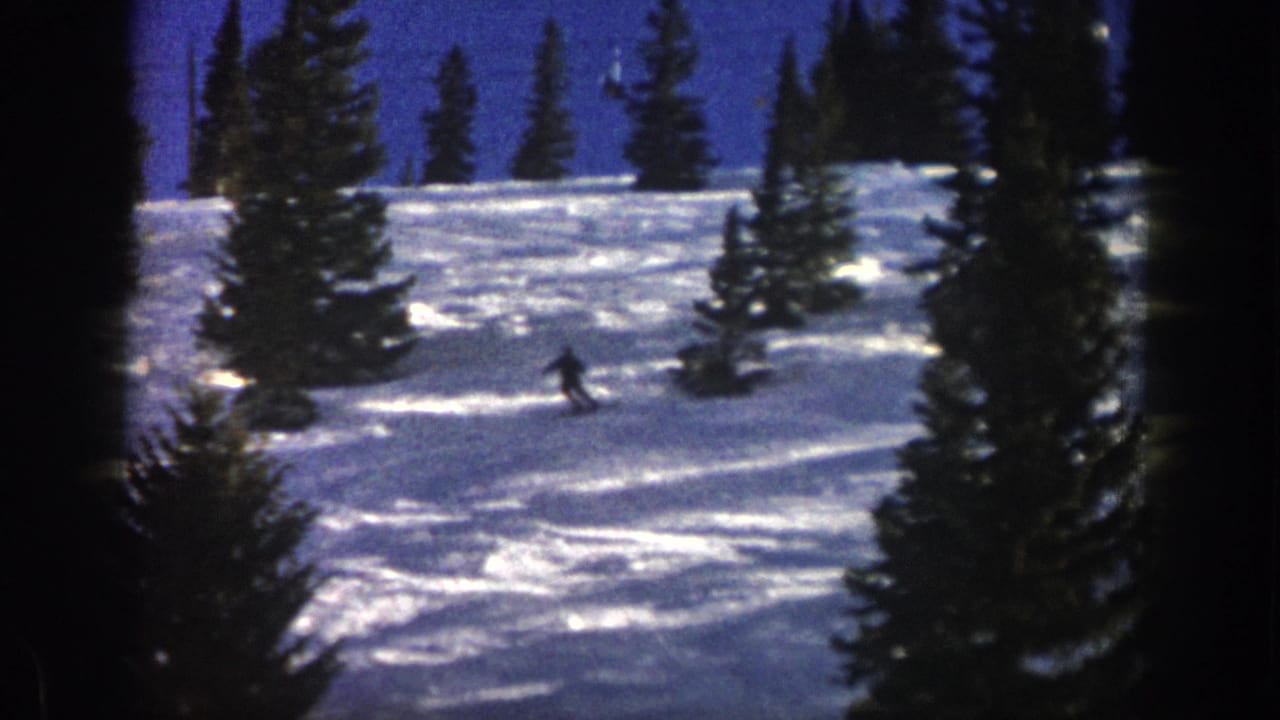 1961 Aspen home-movie frame showing a distant skier descending a snowy slope framed by evergreen trees.