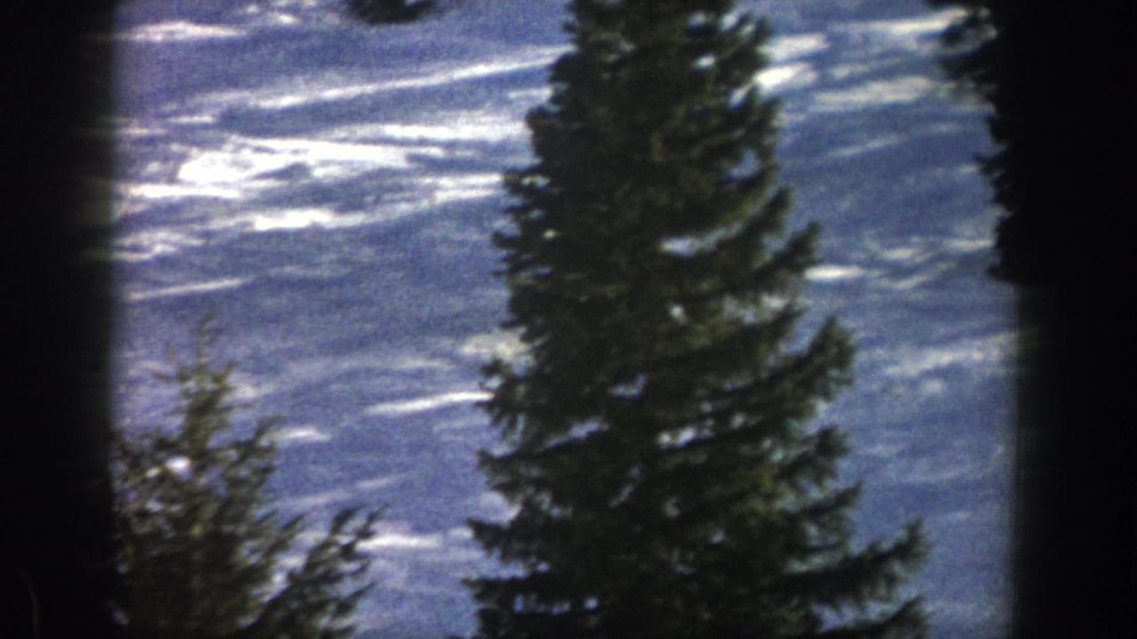 Aspen snowfield and tall evergreens fill the frame, with ski tracks and glare visible in the 1961 8mm footage.