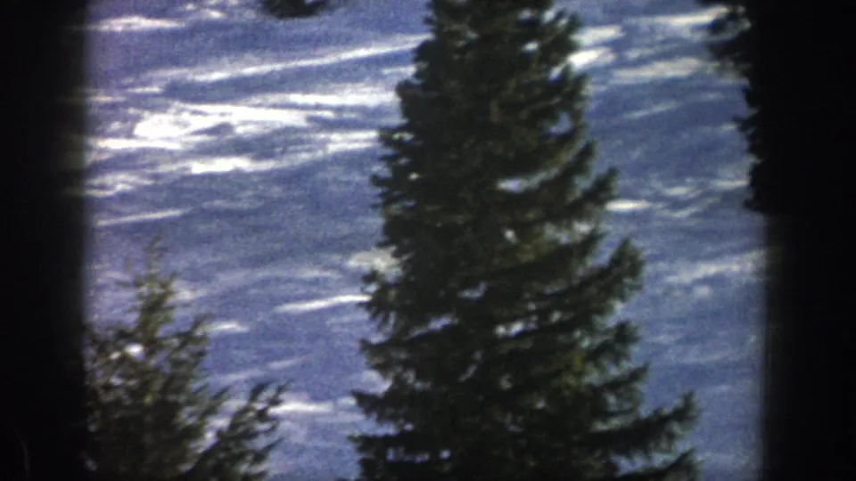 Aspen snowfield and tall evergreens fill the frame, with ski tracks and glare visible in the 1961 8mm footage.