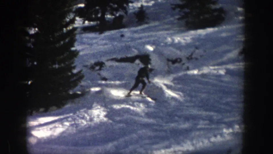 A lone skier descends near evergreens on an Aspen, Colorado slope in 1961 8mm home-movie footage.
