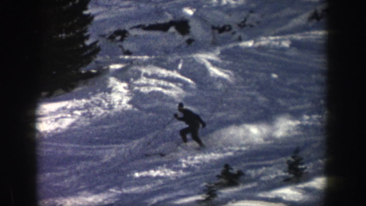 A skier turns across a bright patch of snow on a wooded slope.