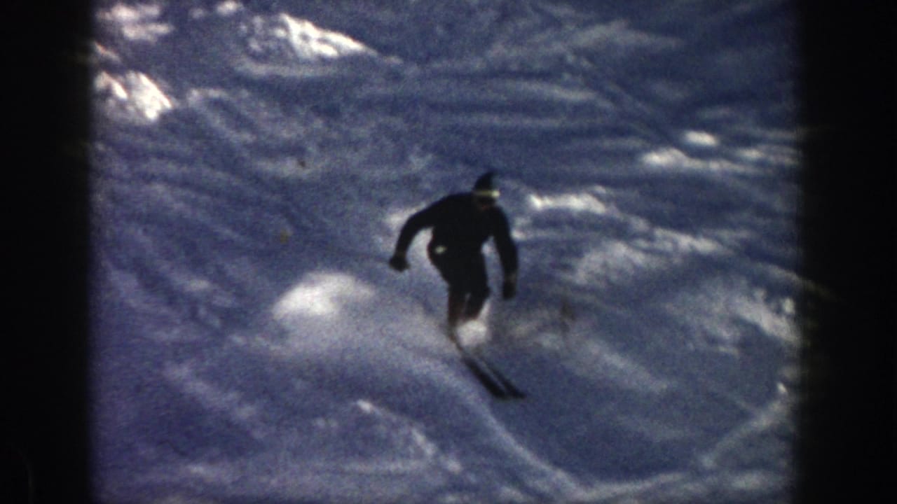 In 1961 Aspen, a lone adult skier moves downhill through a snowy ravine, filmed from a handheld 8mm home-movie viewpoint.