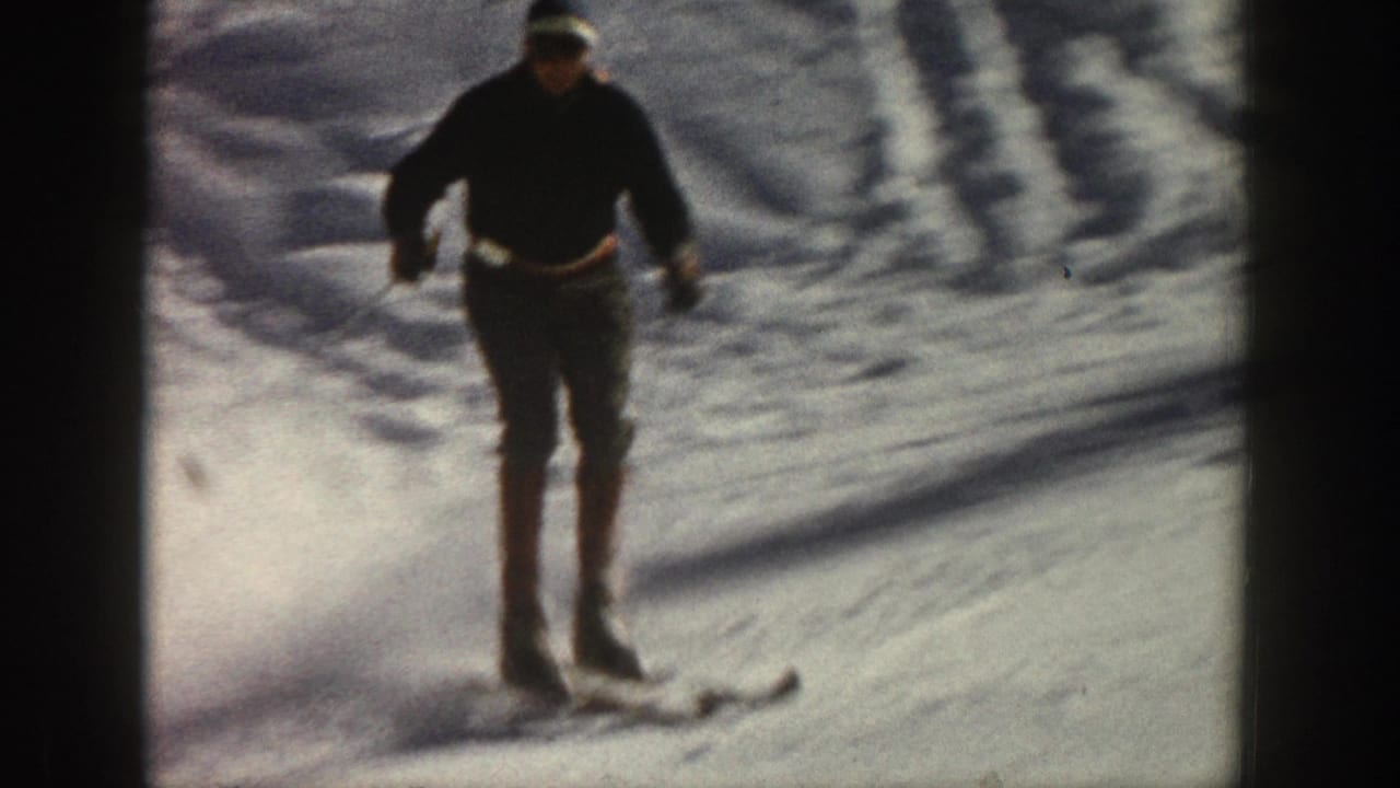 The adult skier approaches in dark winter clothing, using poles as the handheld 8mm camera frames the snowy Aspen slope.