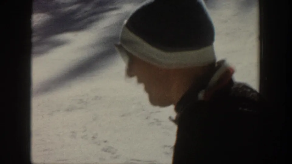 The skier passes near the 8mm camera in profile, with cap and sunglasses visible against the snowy Aspen slope.