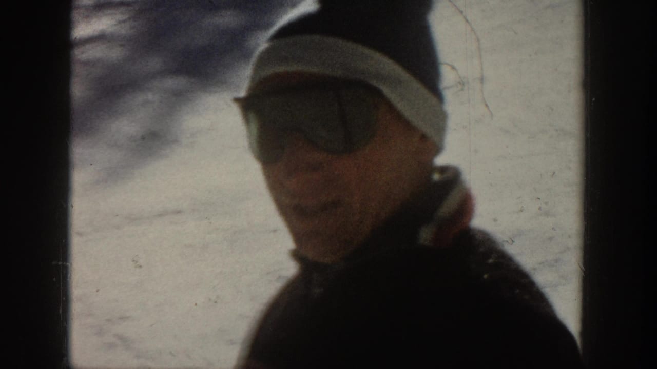 1961 Aspen home-movie frame showing a person in profile wearing sunglasses and a dark beanie near a snow-bright window.