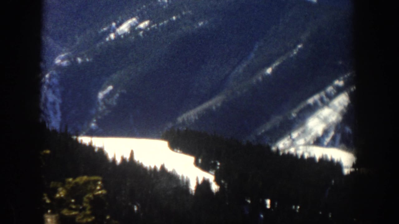 Aspen, Colorado winter mountain view through a window, with bright snowfields, dark tree line, and soft 8mm exposure.