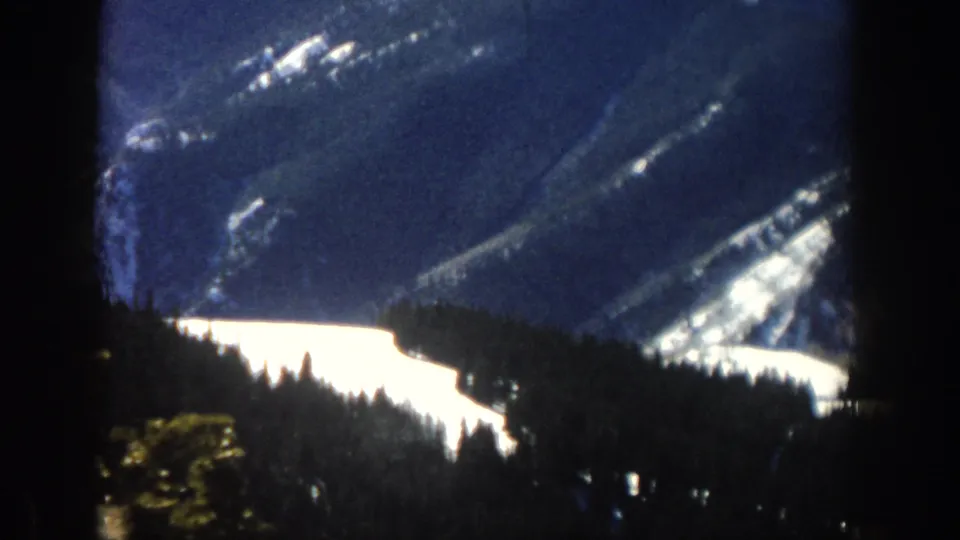 Aspen winter scenery seen through a window, with snowfields, forested slopes, and high-contrast 8mm home-movie exposure.