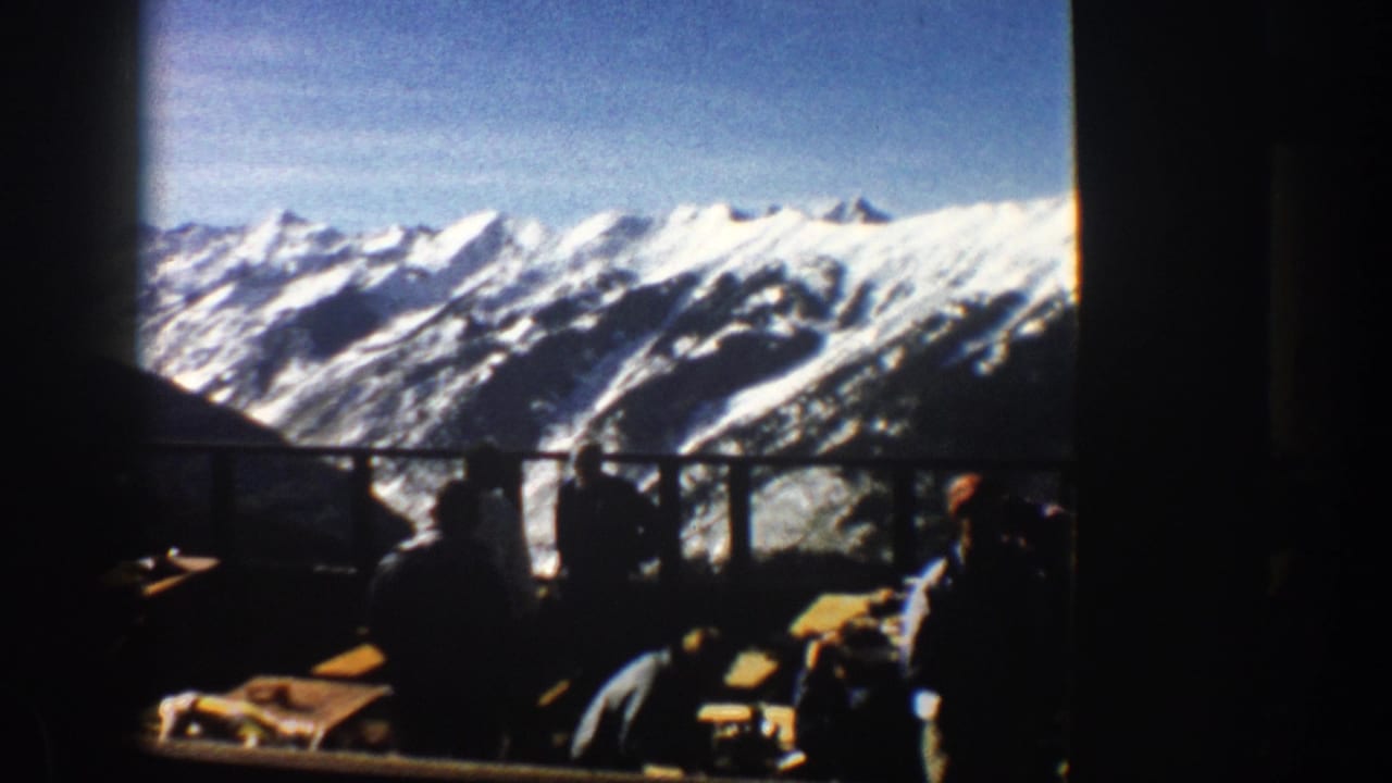 Seated guests in silhouette beside tables with snowy mountains beyond the windows.