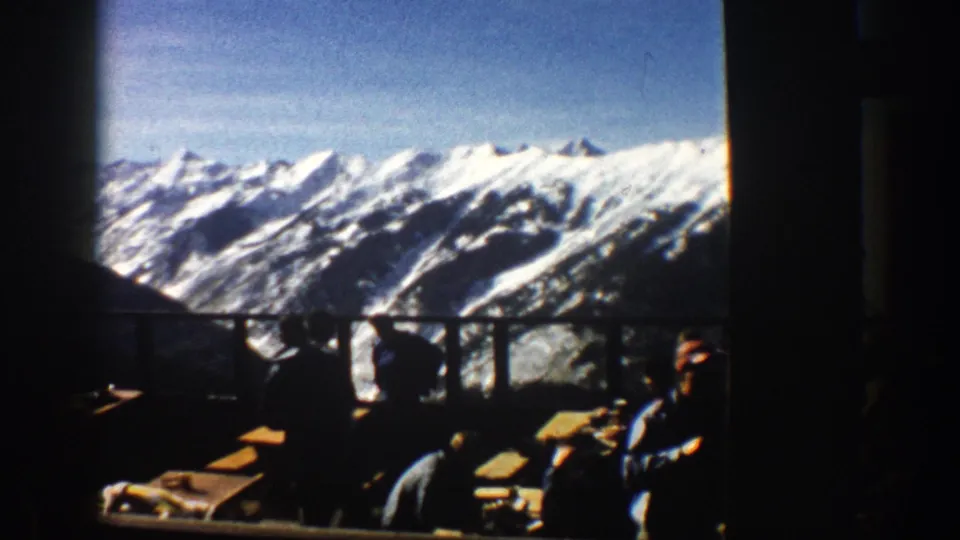 A wide 8mm view from the lodge shows Aspen-area snowy ridges beyond window rails, with seated visitors partly visible in shadow.
