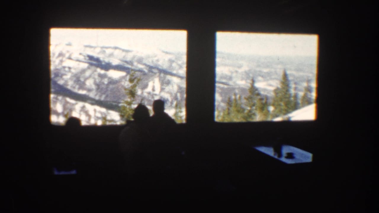 Dark interior with silhouetted visitors facing large windows and snowy peaks outside.
