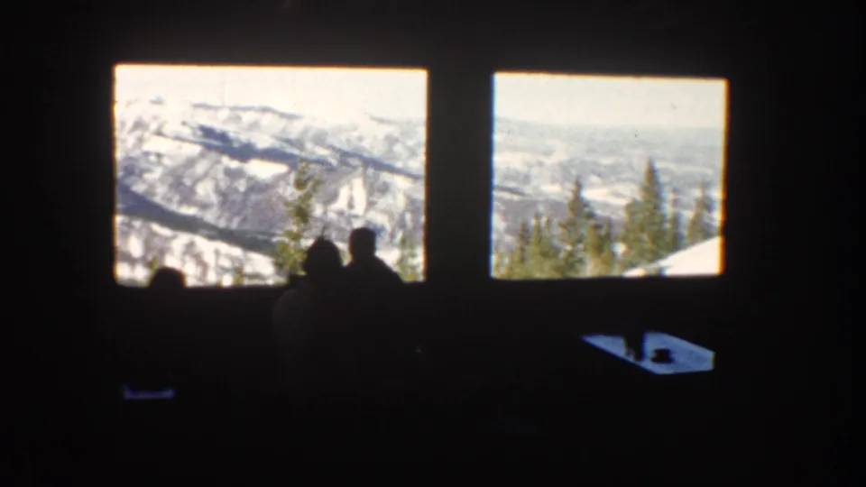 Aspen restaurant interior with seated silhouettes framed by large windows looking toward snowy ridges and evergreen trees.
