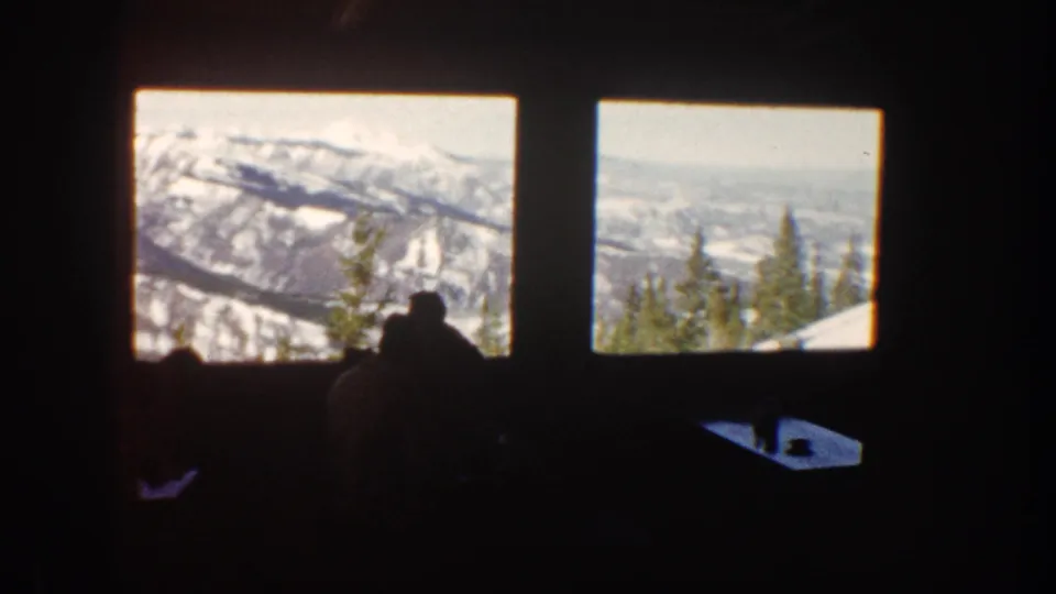 Aspen home-movie frame of restaurant guests in silhouette against large windows and a sunlit Colorado mountain panorama.