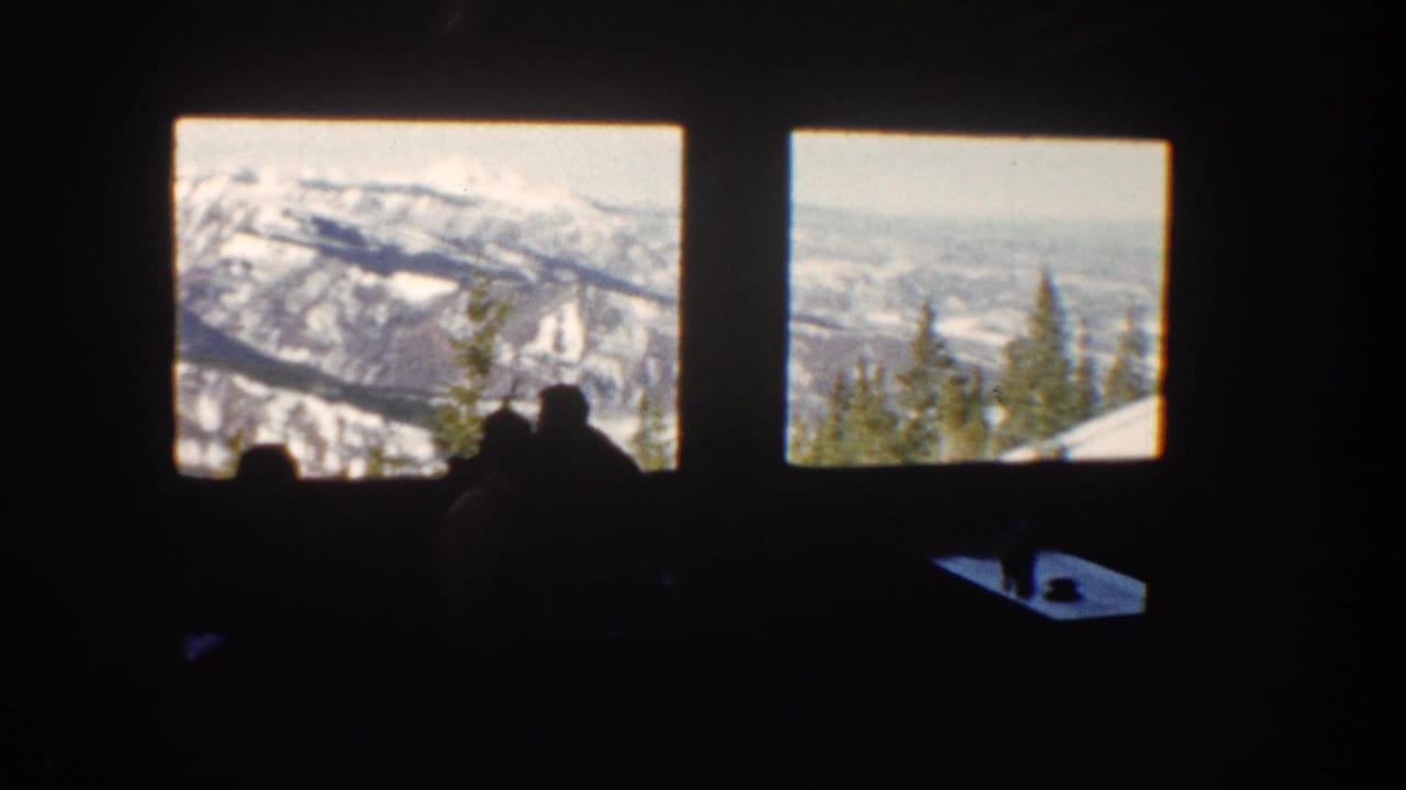 1961 Aspen lodge or restaurant interior with silhouetted visitors looking out at snow-covered mountains through large windows.