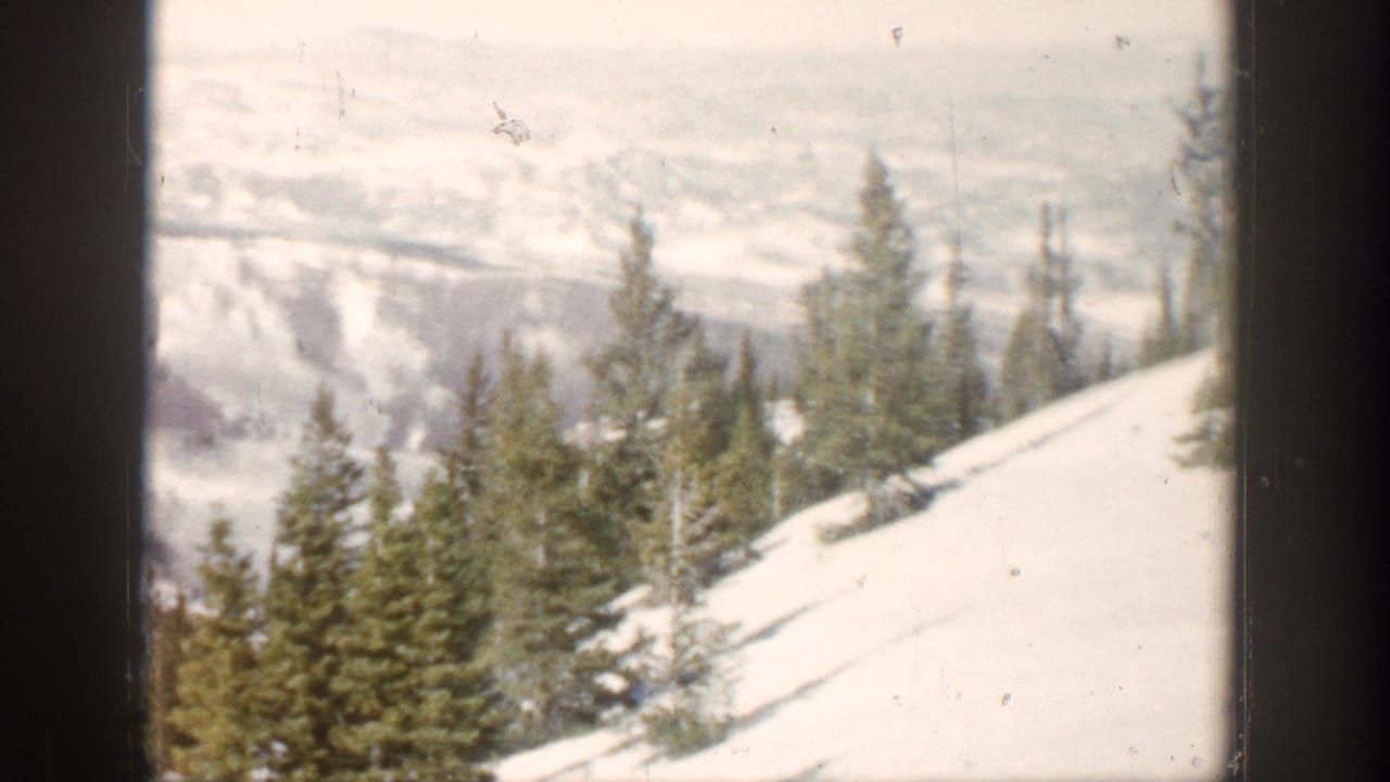 Snow-covered Aspen hillside with pine trees in the foreground and hazy mountain ridges beyond.