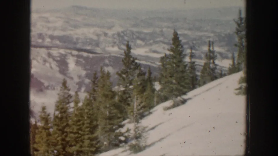 Aspen winter landscape showing pines on a snow-covered hillside with layered mountain ridges in the background.