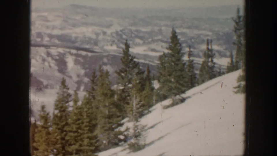Snowy Aspen mountain view with pines and distant ridges, partially framed by dark lodge window edges.