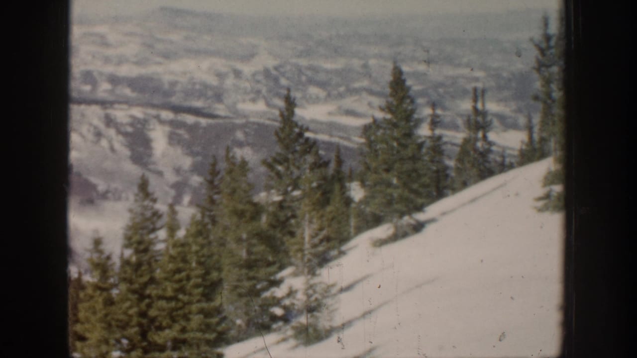 1961 Aspen-area 8mm view of evergreen trees on a snowy slope with distant valley terrain in the background.