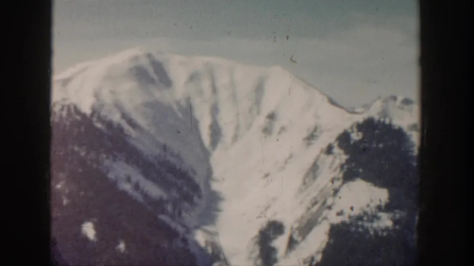 Vintage 8mm view of a broad snow-covered mountain slope with darker forested terrain below.