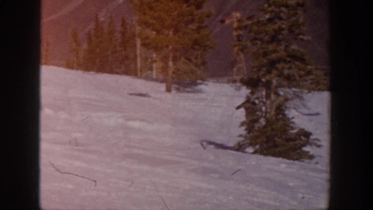 Snowy Aspen ski slope with evergreen trees and mountain background in warm 1961 8mm color.