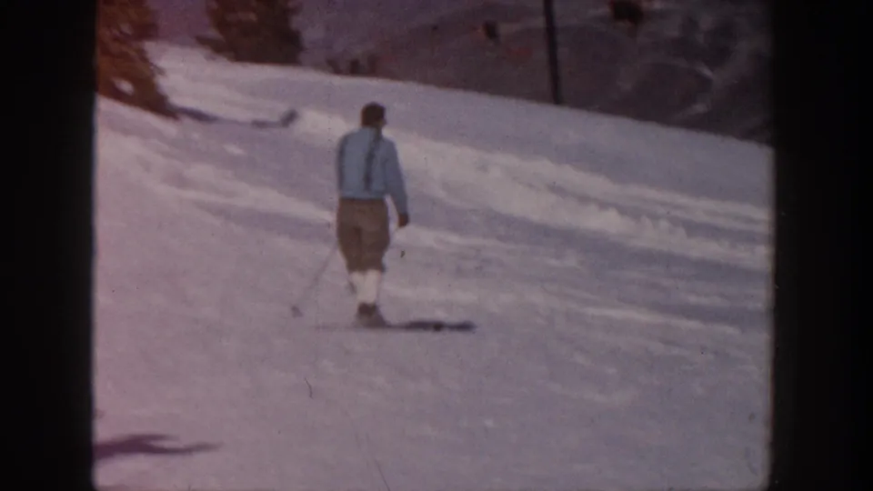 Adult man in a light blue jacket and knickerbocker-style ski trousers moves away on an Aspen snow slope.
