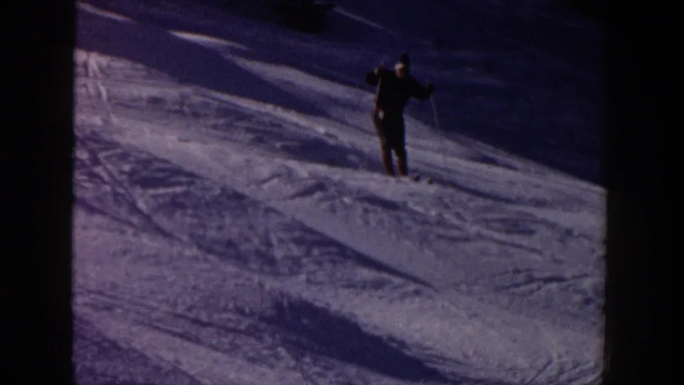 Home-movie frame from Aspen, 1961, showing a skier approaching on a darker section of snow with long shadows.