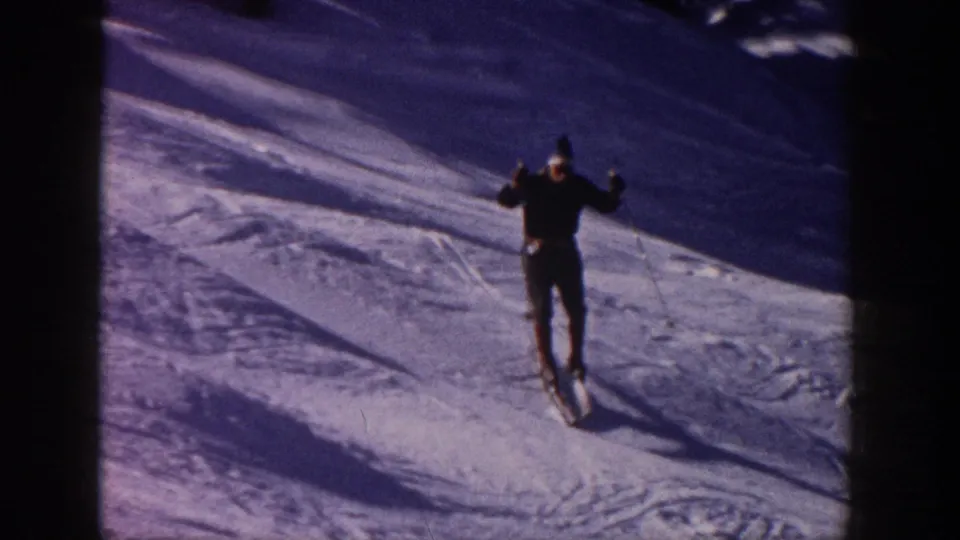 1961 Aspen frame showing a skier near the camera on skis, with poles raised and strong shadows across the snow.