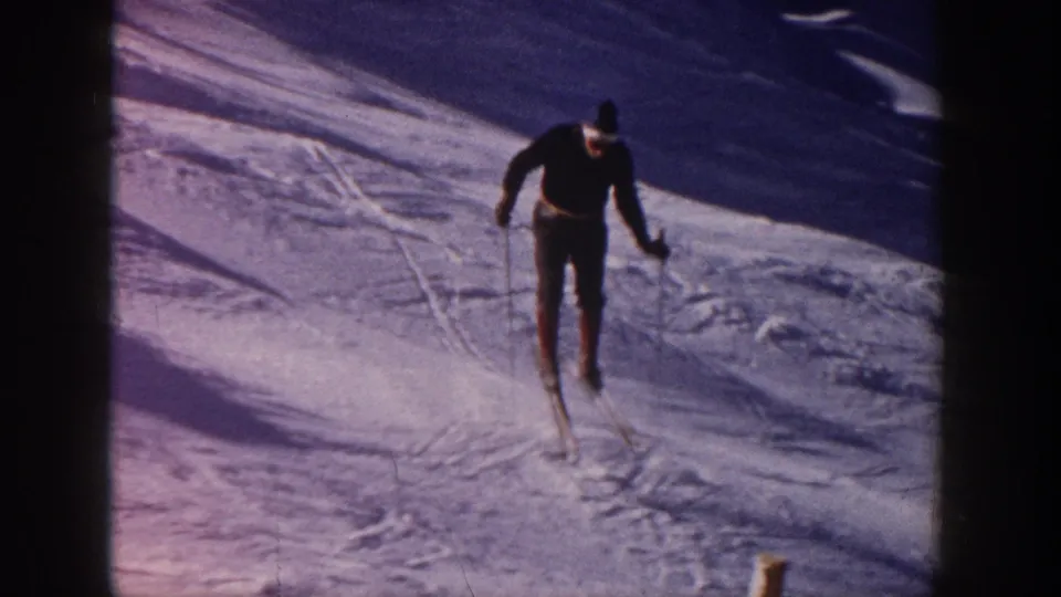 Male skier on a snowy Aspen slope in 1961 home-movie footage, moving downhill through visible ski tracks.
