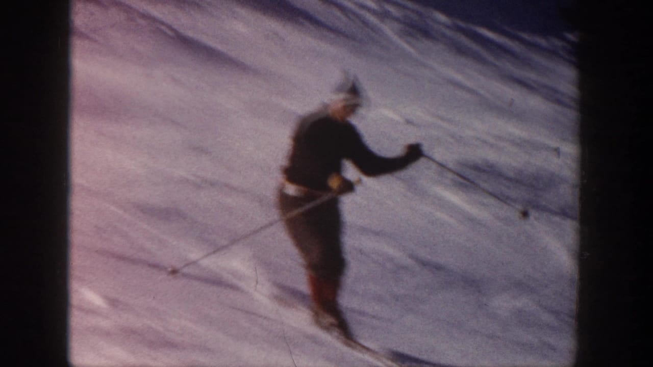 The skier crosses the snowy slope in profile, wearing dark winter clothing and a knit cap in the 1961 Aspen footage.