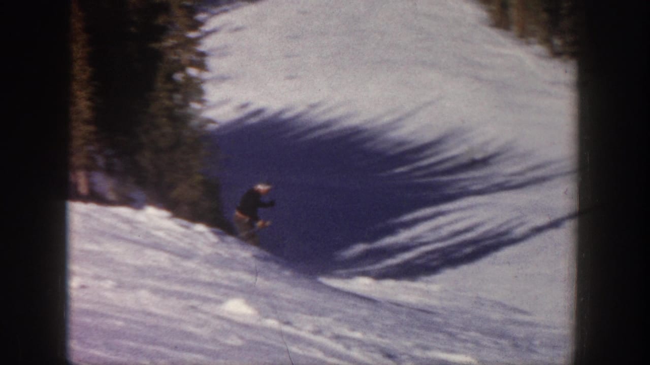 A distant skier moves down a snowy Aspen slope in 1961 home-movie footage, with evergreen trees and blue winter shadows nearby.