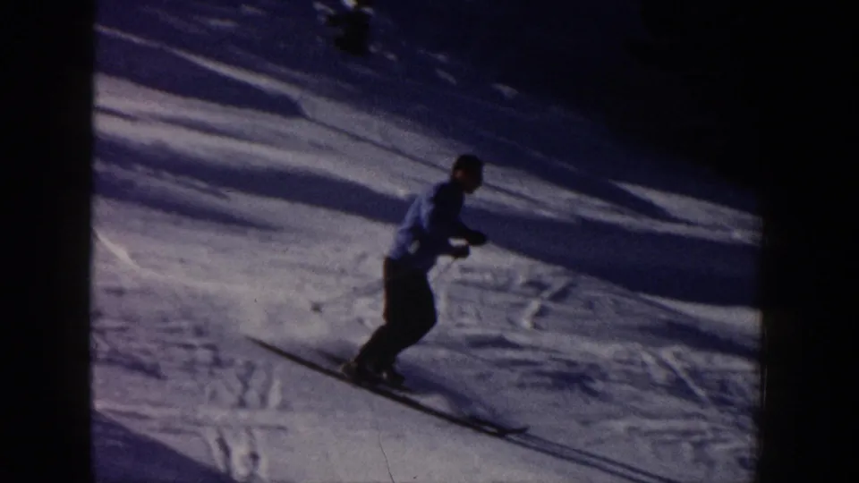 A closer view shows a skier in a light jacket and dark pants gliding across shadowed Aspen snow in 1961 8mm footage.