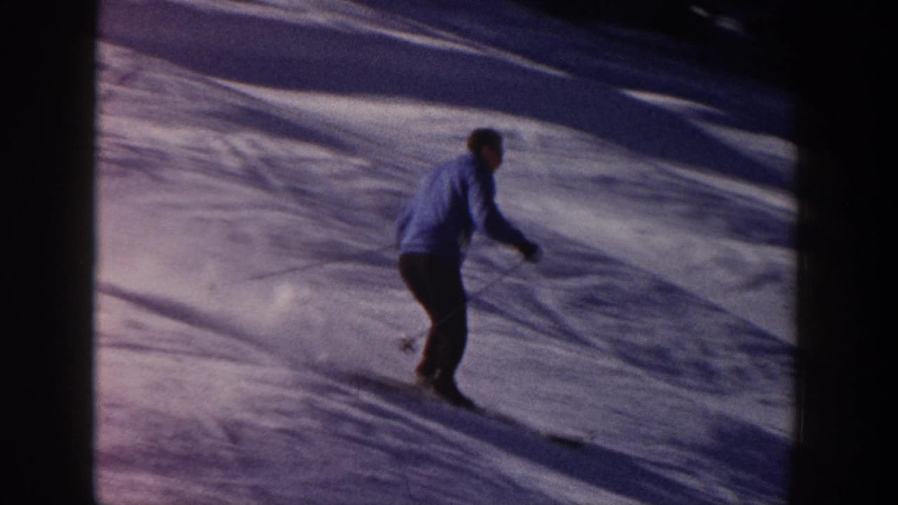 Adult skier in a blue jacket and dark pants descends a snowy Aspen slope in 1961 8mm home-movie footage.