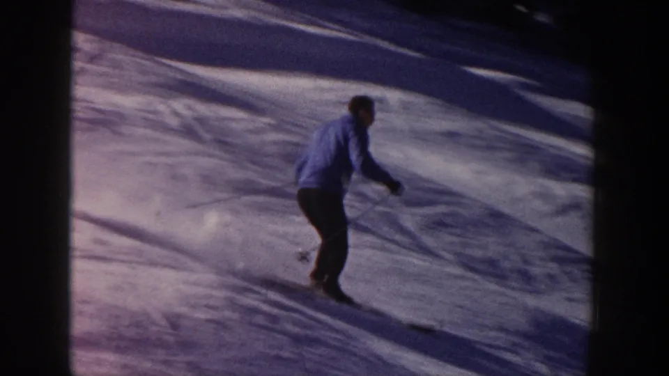 Adult skier in a blue jacket and dark pants descends a snowy Aspen slope in 1961 8mm home-movie footage.