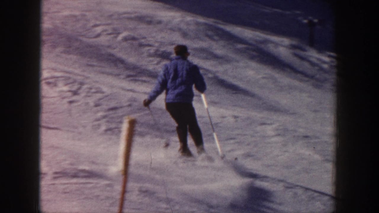 Skier viewed from behind continues downhill on an Aspen snow slope, with poles planted and powder lifting behind him.