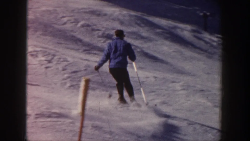 Skier viewed from behind continues downhill on an Aspen snow slope, with poles planted and powder lifting behind him.