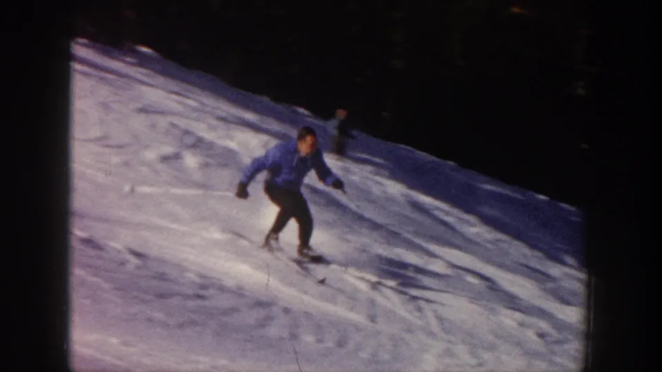 Adult skier in a blue jacket and dark pants moves downhill on a snowy Aspen slope in 1961 home-movie footage.