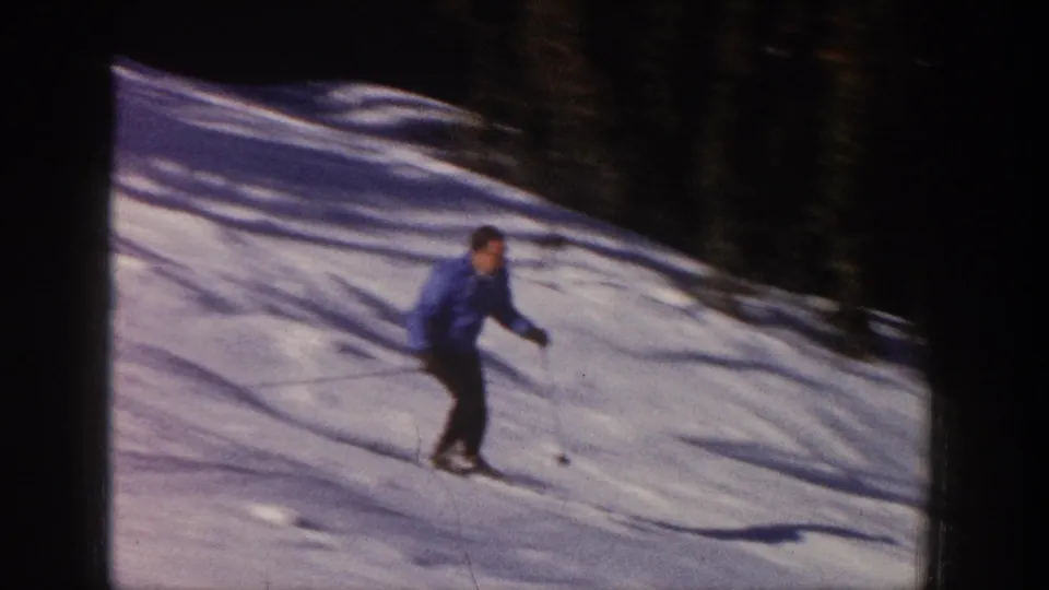 A lone skier crosses a snowy Aspen slope, with dark evergreens and long shadows visible in the 8mm frame.