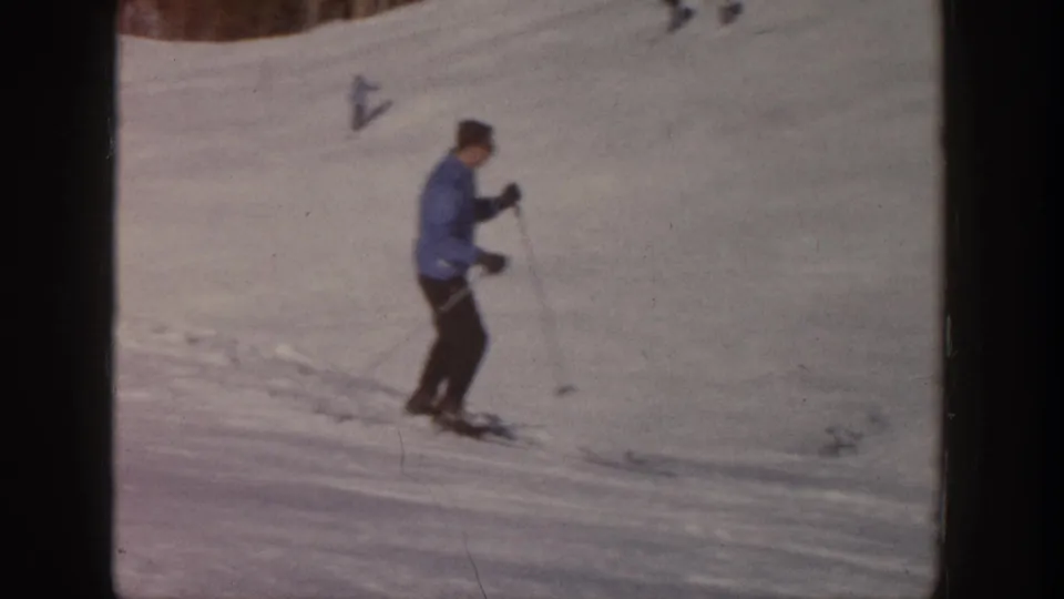 The adult skier appears to slow on the open snowy Aspen slope, holding ski poles in a soft 1961 8mm frame.