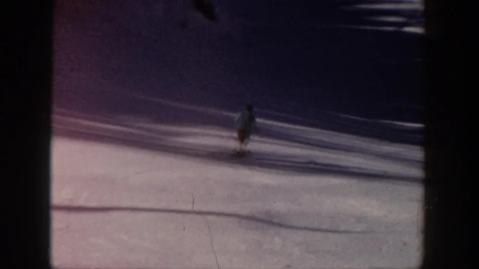 A distant skier moves through a darker band of shadow on the snowy Aspen slope in this 1961 8mm frame.