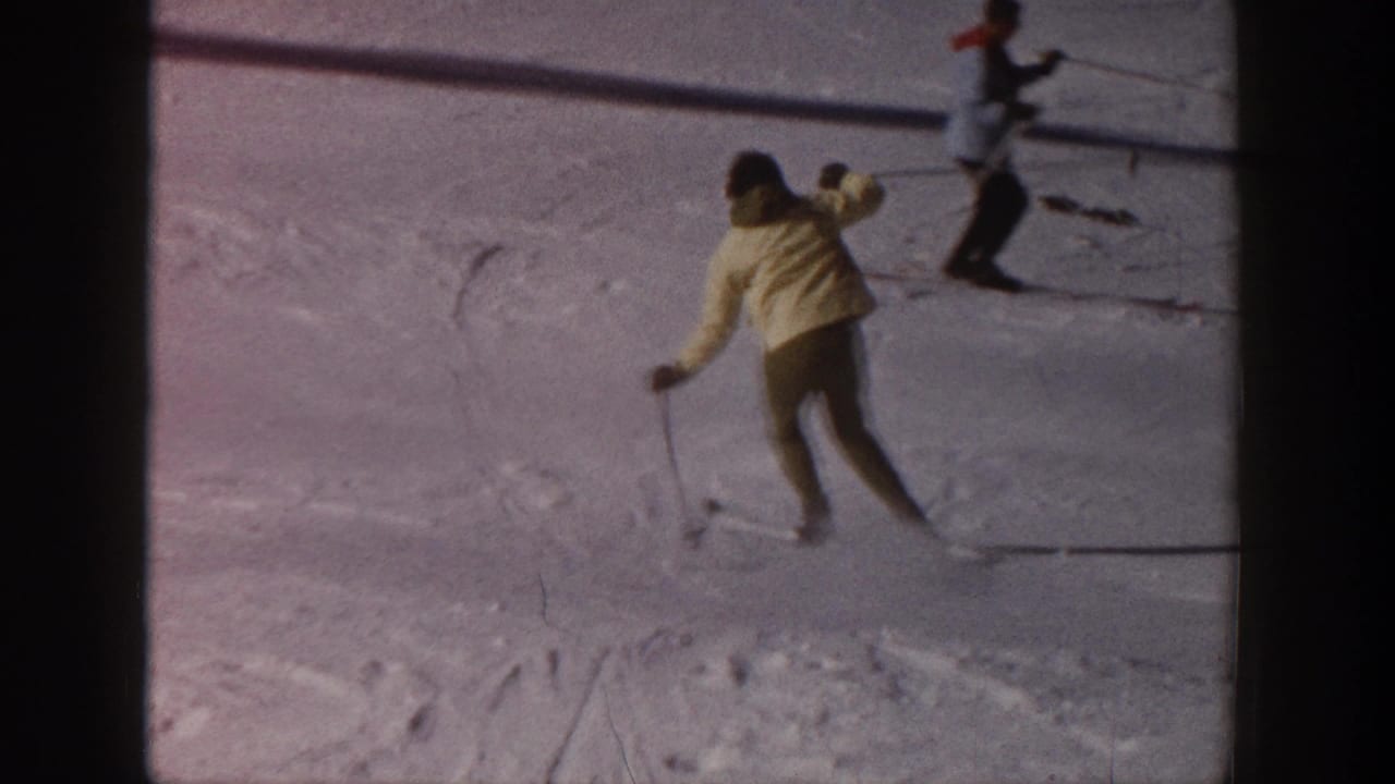 Skier in a light jacket moves downhill on a snowy slope with another skier nearby.
