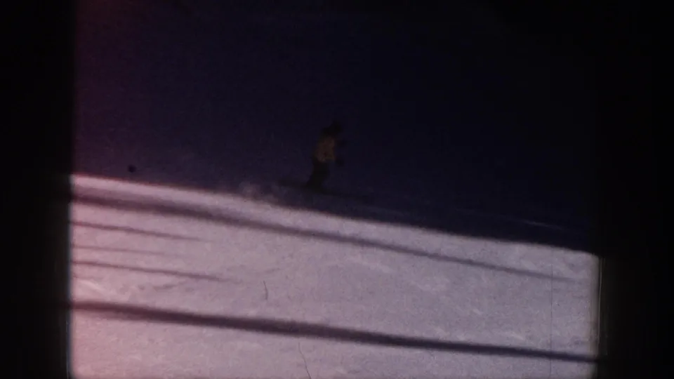 A distant skier continues downhill into deep shadow on the Aspen snow slope in grainy 1961 8mm footage.