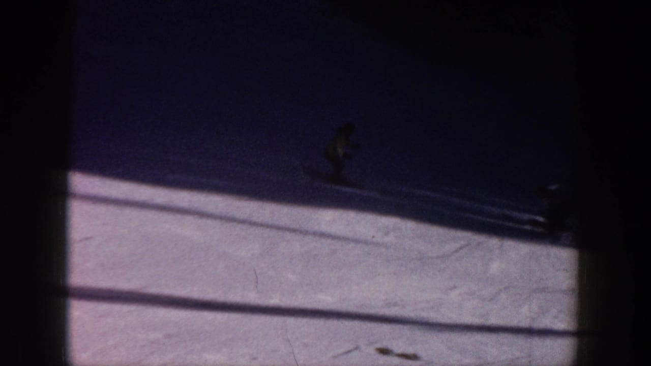 1961 Aspen home-movie frame with a distant skier crossing white snow under dark shadows and visible 8mm frame edges.
