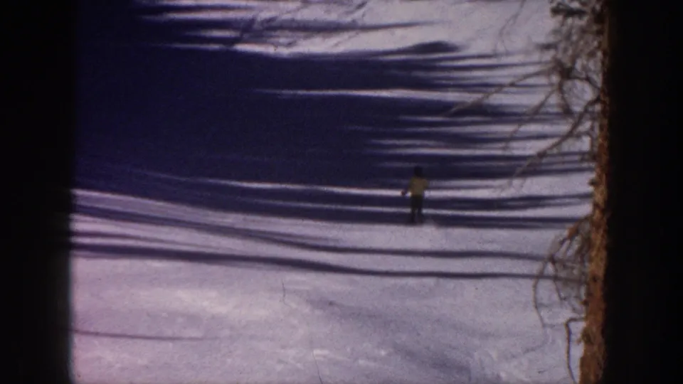 Distant skier on an Aspen snowy slope, with bare tree shadows stretching across the 1961 8mm frame.