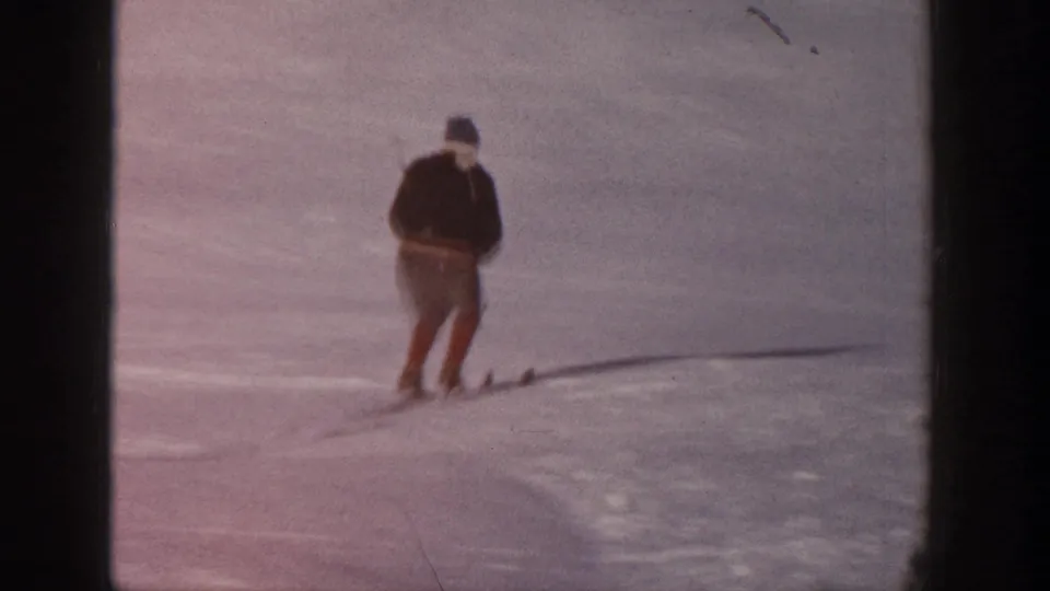 A skier in dark winter clothing and hat glides across the snowy Aspen slope in the 1961 home-movie frame.