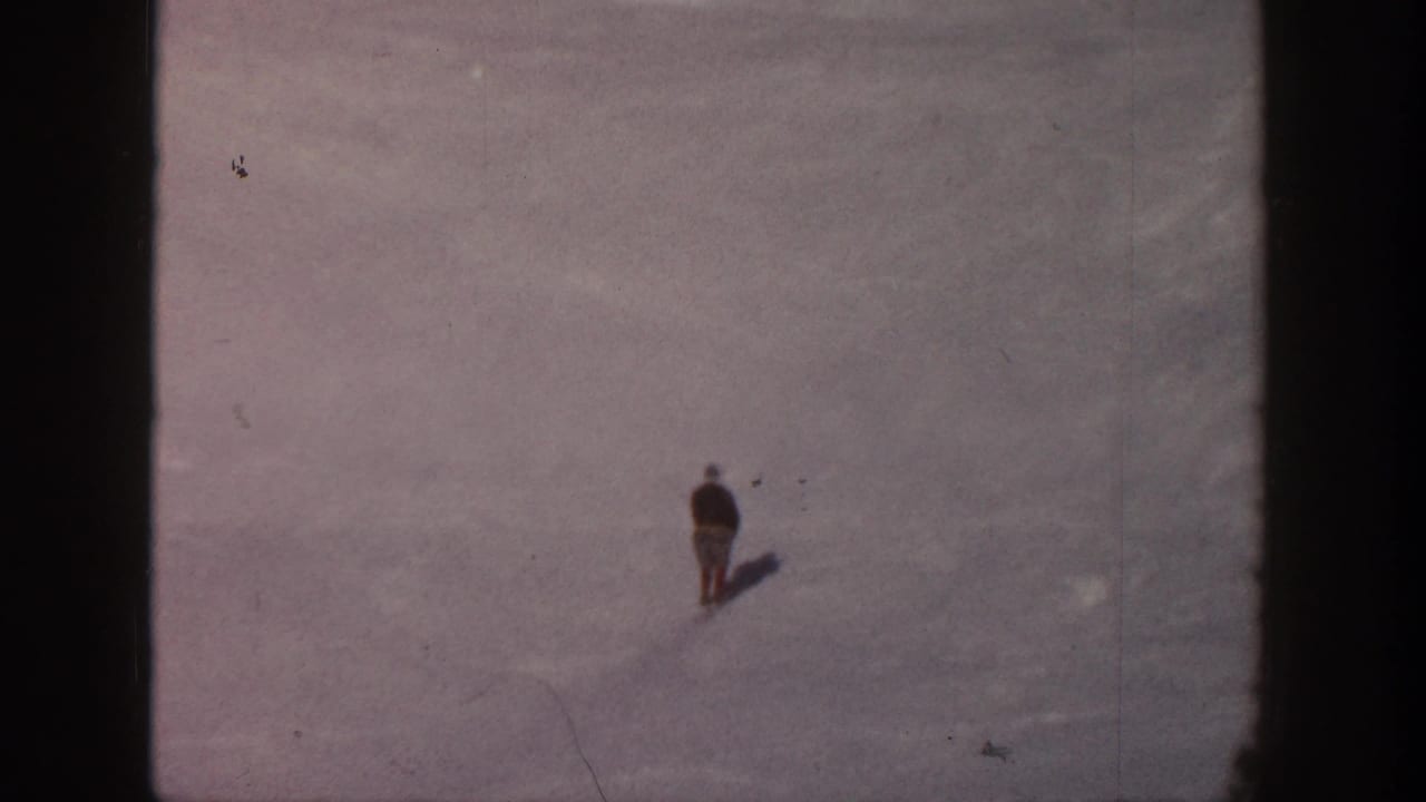 Small skier moving across a wide snowfield with a shadow behind them.