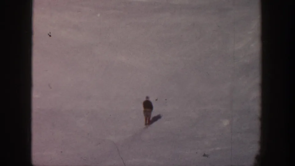 A lone skier in the Aspen snowfield moves farther downslope, their small figure and shadow standing out against pale snow.