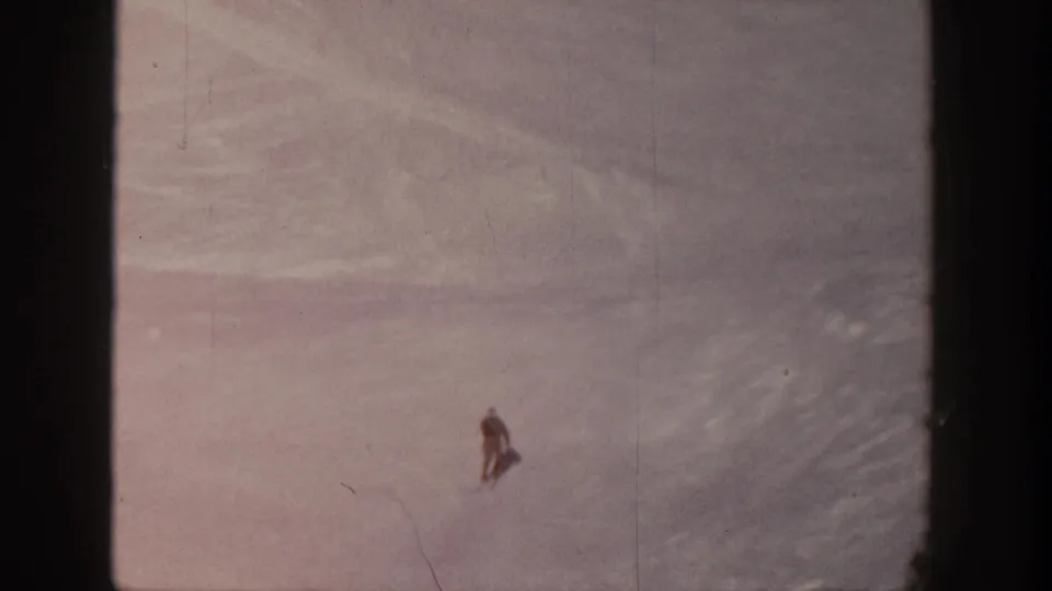 The skier appears low in the frame on the Aspen slope, surrounded by a large expanse of textured snow and visible film wear.