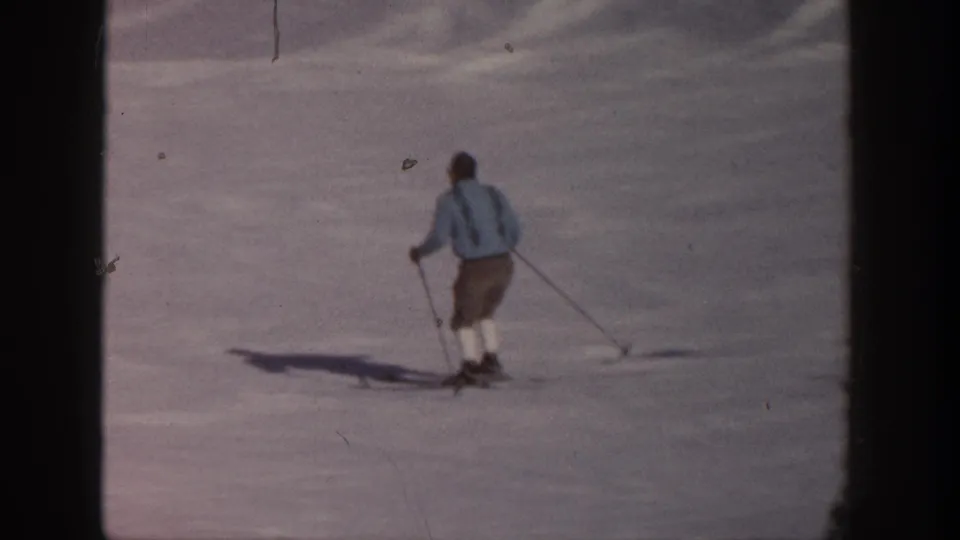 Closer 1961 Aspen home-movie frame of a skier in a light blue jacket using poles while moving downhill on snow.
