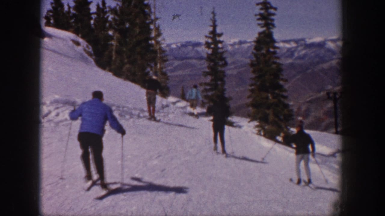 1961 Aspen home-movie frame showing skiers on a snowy slope with evergreen trees and mountain ridges beyond.