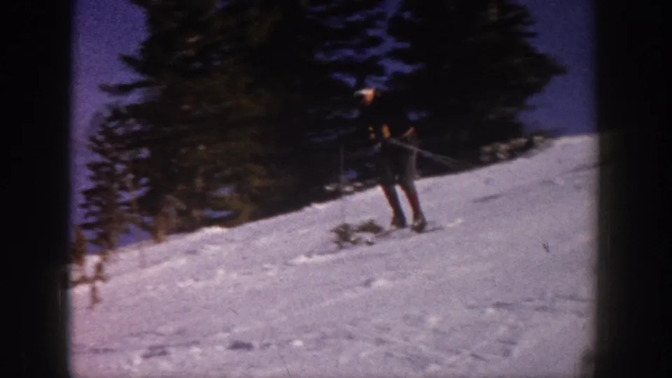 1961 Aspen home-movie frame of a skier on a snow-covered slope below tall evergreen trees.